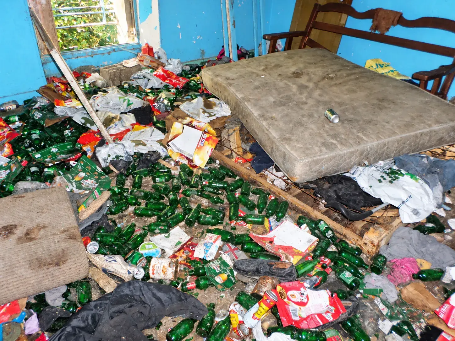 Chambre aux murs bleus, sol couvert de bouteilles vertes et de déchets